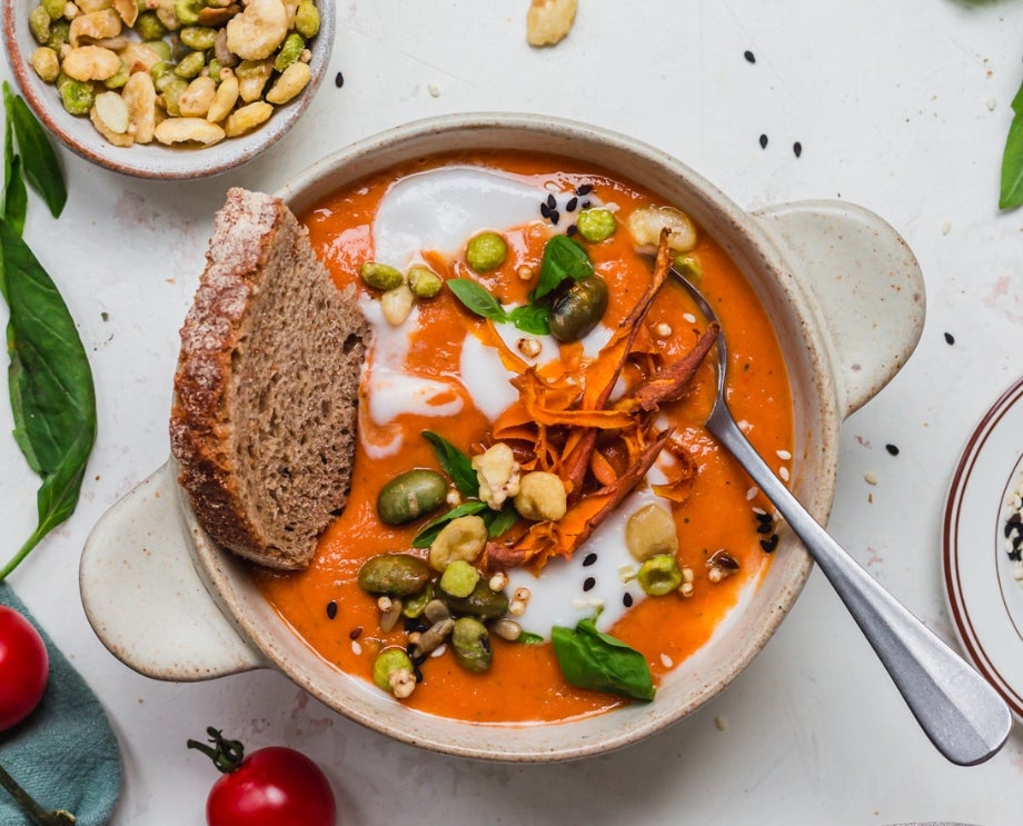 A bowl of tomato soup, with a slice of bread, topped with Nature's Heart's Crunch