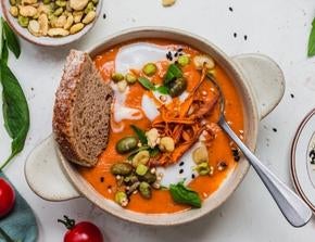 A bowl of tomato soup, with a slice of bread, topped with Nature's Heart's Crunch