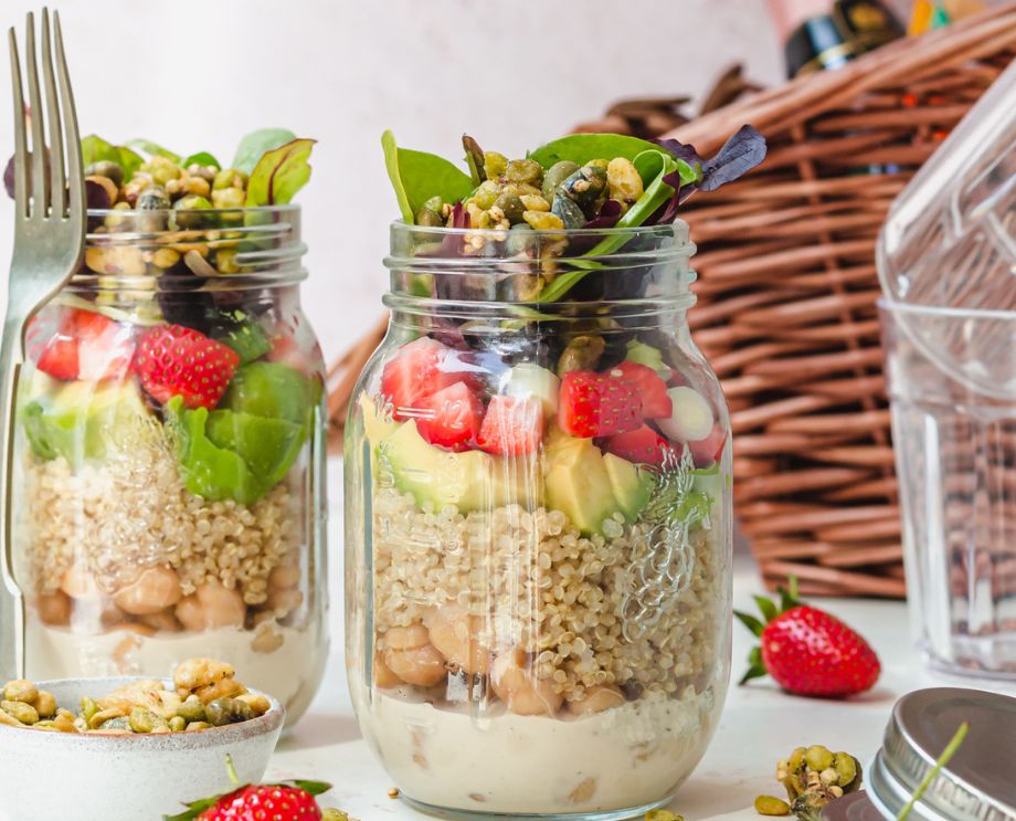 Two jars of strawberry and avocado salad in front of a picnic basket