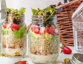 Two jars of strawberry and avocado salad in front of a picnic basket